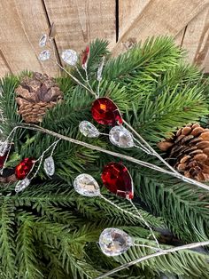 some pine cones and red glass ornaments are on the table next to evergreen branches with needles