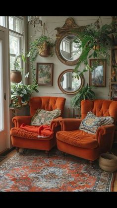 two orange chairs sitting in front of a window with potted plants on the wall