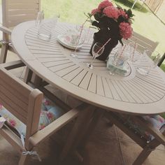 an outdoor table with chairs and vases on it, in the middle of a patio