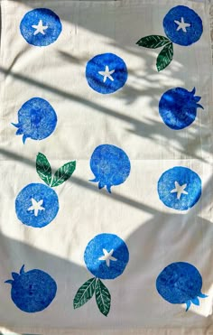 a blue and white table cloth with green leaves on it, in the shape of pomegranates