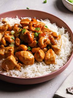 a pink bowl filled with rice and chicken on top of a white table next to silverware