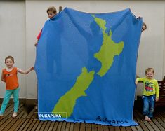 two children holding up a blue and green blanket with the map of new zealand on it