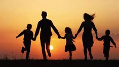 a family holding hands while walking across a field with the sun setting in the background