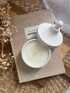 a white candle sitting on top of a wooden table next to a basket with dried flowers