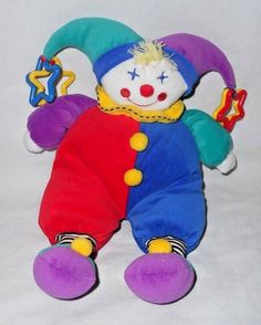 a colorful clown stuffed animal sitting on top of a white sheet covered ground with stars