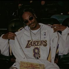 a man sitting in a chair with his hands on his hips wearing sunglasses and a lakers jersey