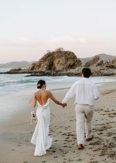 a bride and groom holding hands walking on the beach with their dog in tow at sunset