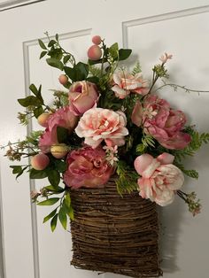 a basket filled with lots of pink flowers on top of a wooden door handle next to a white door