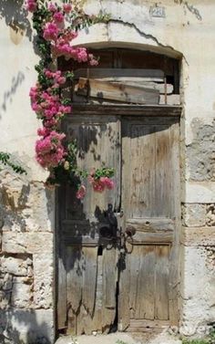 an old wooden door with pink flowers growing out of it's frame and on the outside