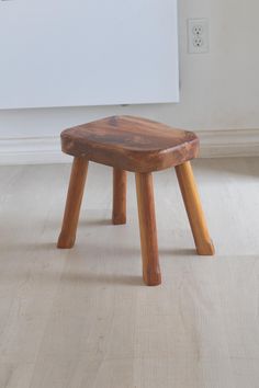 a wooden stool sitting on top of a hard wood floor next to a white wall