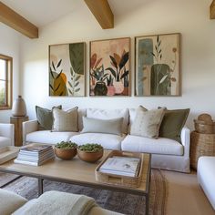 a living room filled with white furniture and paintings on the wall above it's coffee table