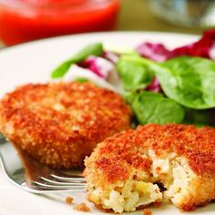 two crab cakes on a white plate with a fork and spinach salad in the background