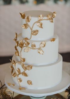 a three tiered white cake with gold leaves on the top and bottom, sitting on a plate