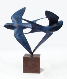 a metal sculpture on a marble base with two birds flying over it's head