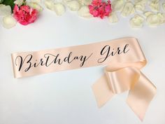 a pink ribbon with the words birthday girl on it next to some flowers and petals