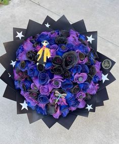 a bouquet of purple and black flowers with a yellow teddy bear on top is shown