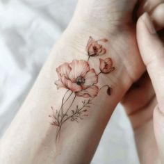 a woman's wrist tattoo with red flowers on her left hand and an orange flower in the middle