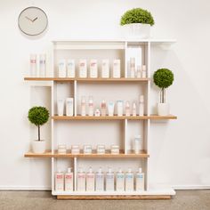 the shelves are filled with different types of skin care products and plants in front of a wall clock