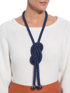 a woman wearing a white sweater and brown pants with a blue rope necklace on her neck