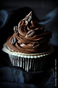 a cupcake with chocolate frosting and coffee beans on top, sitting on a black cloth