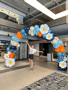 a woman standing in front of a giant balloon arch with flowers and balloons on it