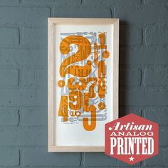 an orange and gray print hanging on a brick wall next to a red sign with the words artisan analog printed