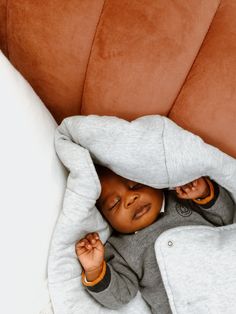 a small child laying on top of a couch covered in a blanket and covering itself