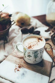 a cup of hot chocolate sitting on top of a wooden table next to an apple