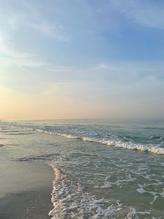 the ocean waves come in to shore as the sun is setting over the horizon and blue sky