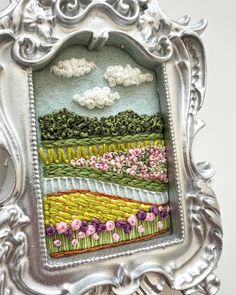 an ornate silver frame with a painting of flowers in the middle and clouds above it