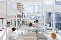 three people sitting on the floor in a room with white walls and windows, while one person works on a laptop