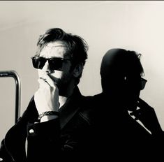 a man wearing sunglasses is sitting in front of a mirror with his hand on his chin