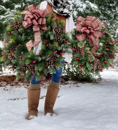 a woman holding a wreath in the snow with pine cones and red berries on it