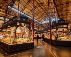 an indoor market with lots of food and people walking around it in the evening time