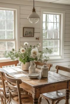 a wooden table topped with vases filled with flowers next to two chairs and a window