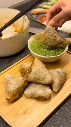 a person dipping some food into a bowl on top of a cutting board next to other foods