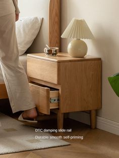 a person standing next to a bed with a night stand and lamp on top of it