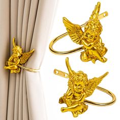 three gold angel napkin rings sitting on top of a white table next to a curtain