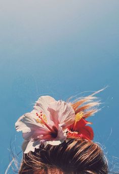 a close up of a woman with a flower in her hair and blue sky behind her