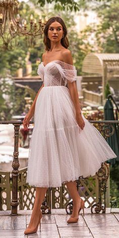 a woman in a white dress standing on a balcony next to a chandelier