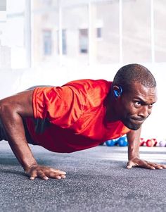 a man in an orange shirt is doing push ups with headphones on his ears