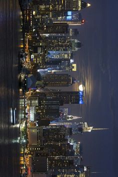 the city skyline is lit up at night with skyscrapers in the foreground and water below