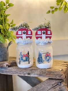 two mason jars decorated with snow and christmas scenes are sitting on a table next to a potted plant