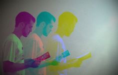 three men are standing in front of a wall with colored images on it and one man is holding a book