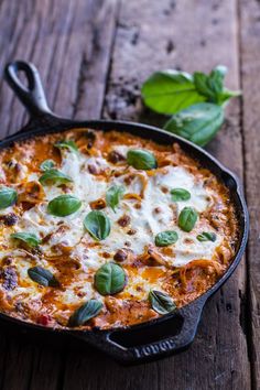 a close up of a pizza in a pan on a wooden table with basil leaves