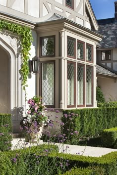 a house that has some bushes in front of it and purple flowers on the side