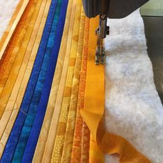 a close up of a sewing machine on a piece of fabric with different colored strips in the background