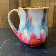 a coffee cup with colorful swirls on it sitting on top of a black table