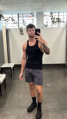 a man taking a selfie with his cell phone in a gym room while wearing shorts and socks