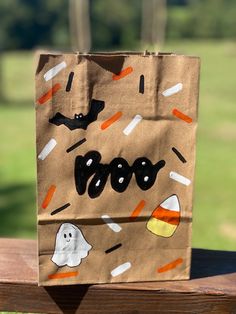 a brown paper bag with halloween candy on it sitting on a wooden bench in the park